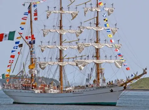 tall ship with two mast with rolled up white sails and colorful flags