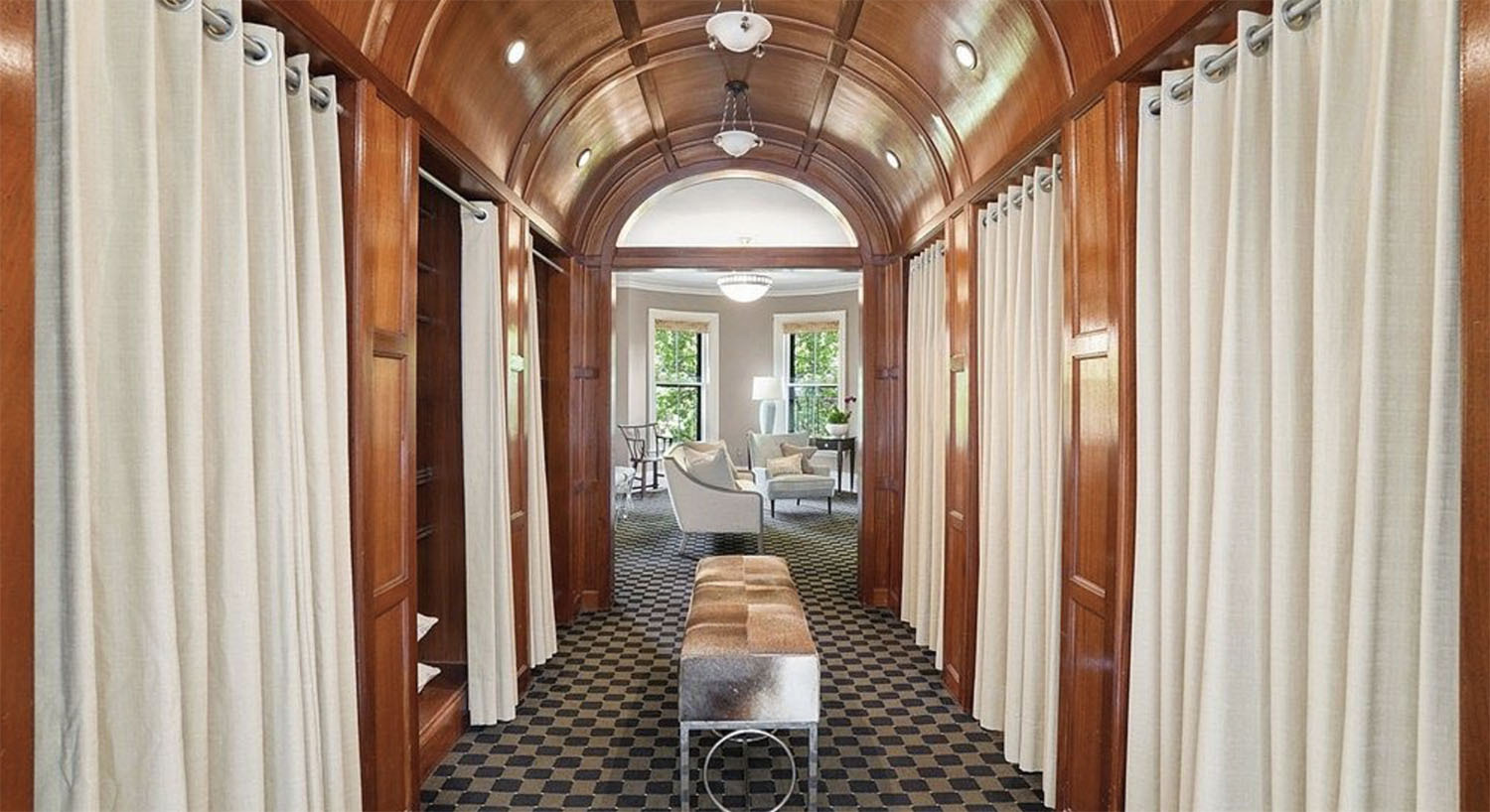 Space with mahogany barrel vaulted ceiling, off white fabric curtains, black and brown carpet, with view of large soaking tub in bathroom