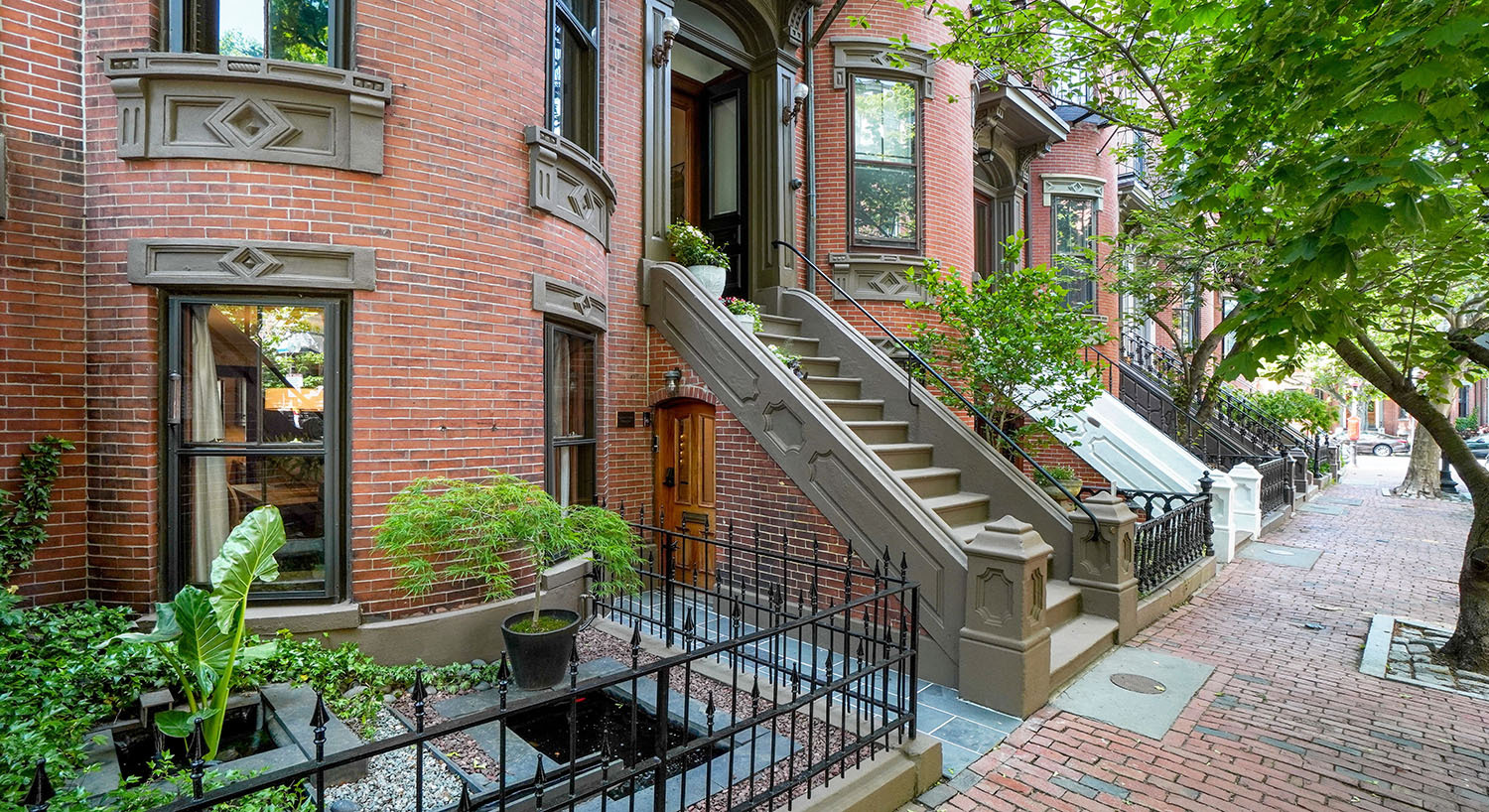 Series of red brick brownstone with big staircase leading to double black front doors