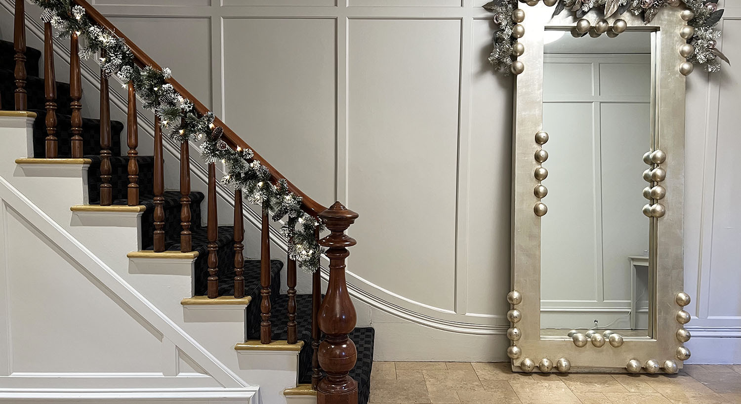 Historic interior staircase, mahogany railing with green garland, large silverleaf wall mirror with matching silver garland.