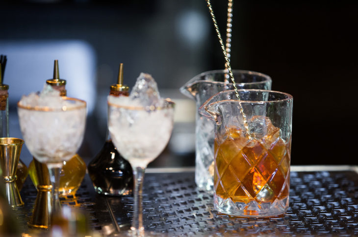 two small chalices with ice and a cross hatched glass with bourbon on a bar