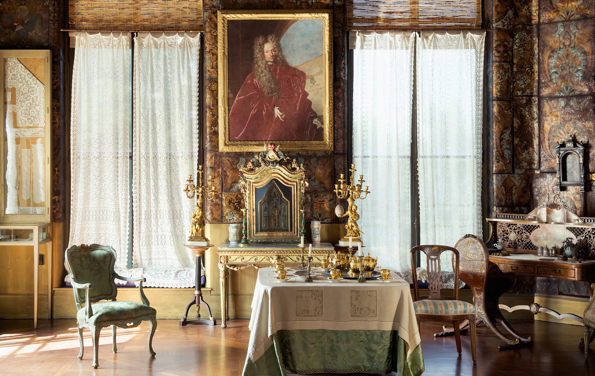 old fashioned room with table with white and green linen and a giant waiting of a man in a red cloak