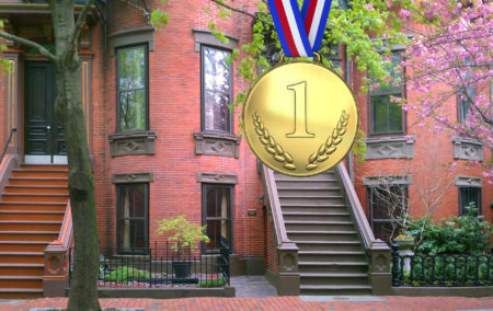 gold medal says number 1 in front of a historic brick townhouse with green leaves of a tree
