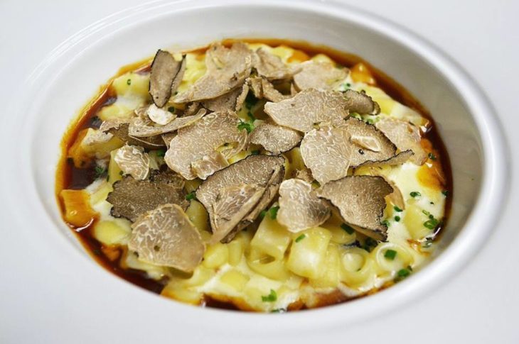 white plate of pasta topped with shaved black truffles