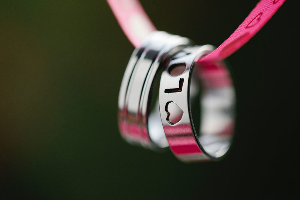 Two silver rings on hanging on a red ribbon with black background. One ring says love on it.