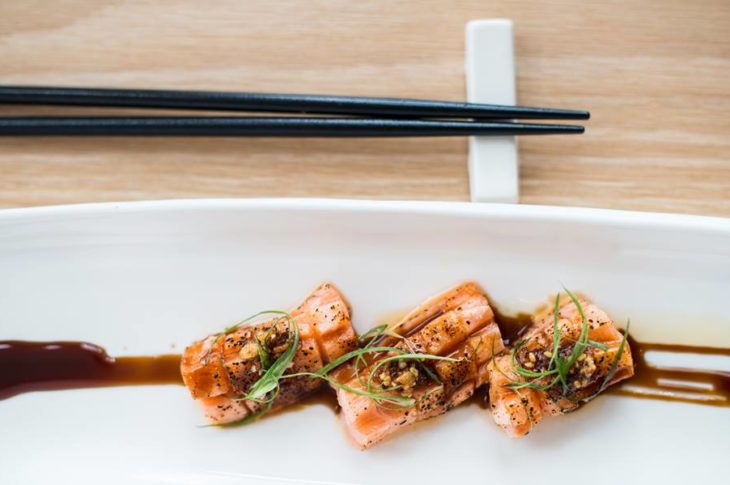 black chopsticks on bamboo mat next to white plate topped with sushi and soy sauce