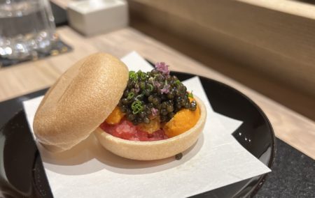 tan rice cup filled with pink tuna and topped with black caviar on a white paper set on a counter that is tan