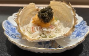 a shell filled with black caviar and orange uni set on a blue and white plate