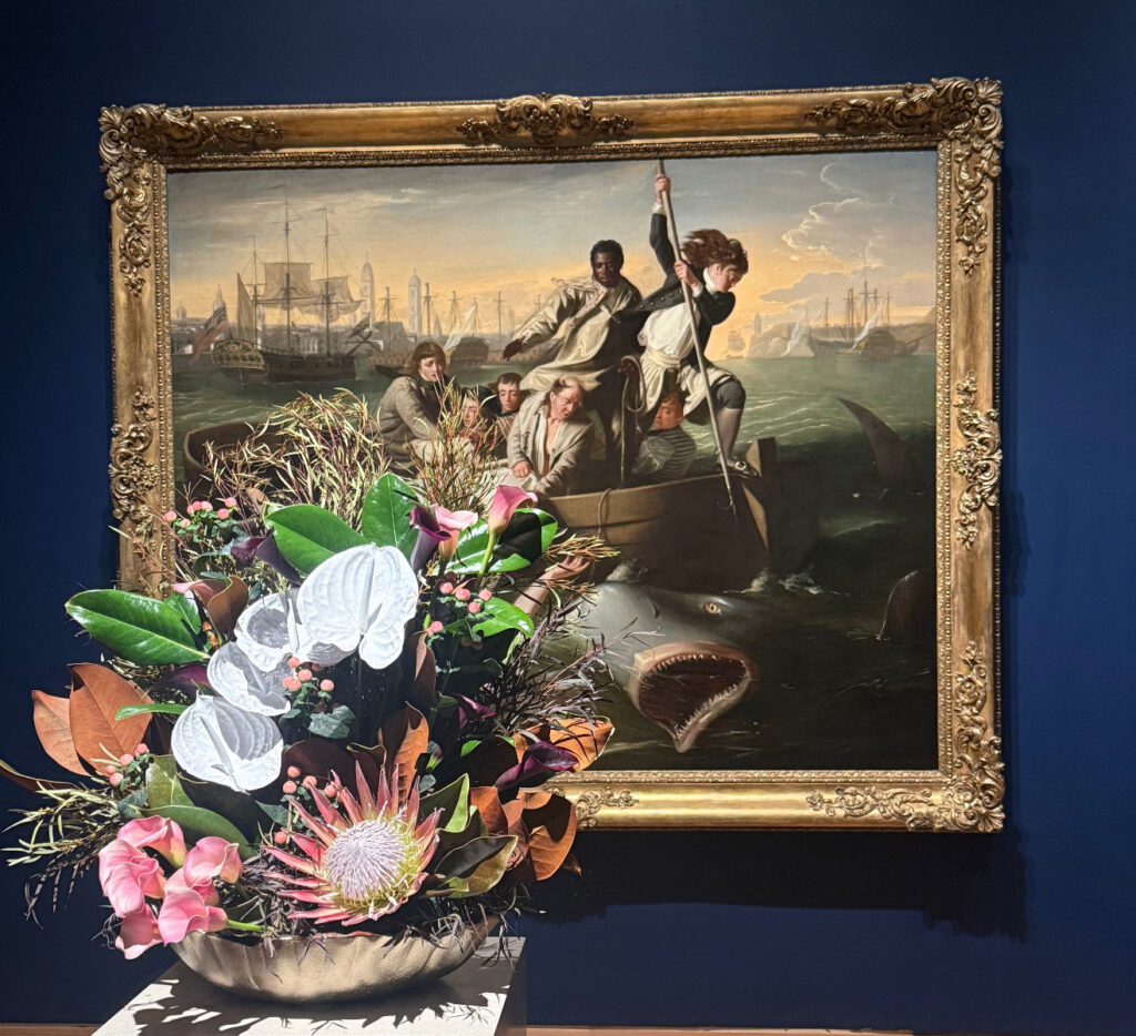 colorful floral arrangement in front of a gold frame with people in a boat and a shark