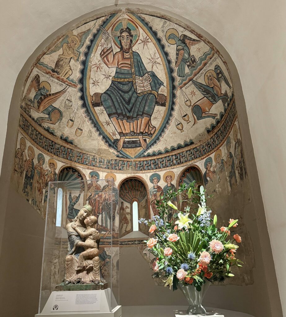 Armenian ceiling fresco in tan blue and pink and statue under class and a floral arrangement
