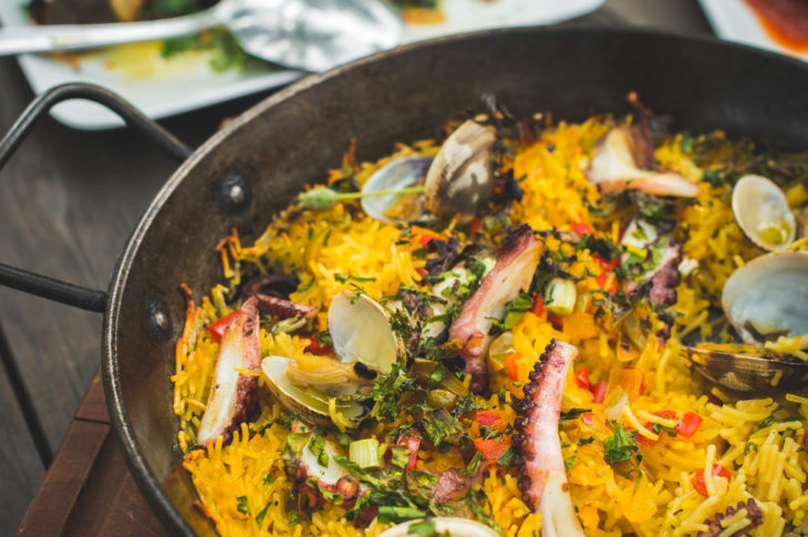 close up pan of yellow paella rice with silver spoon