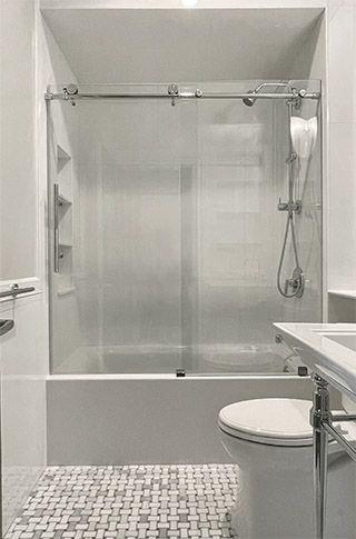 Bathroom with white tub, glass doors, white pedestal sink, bright chrome legs and marble mosaic floor.