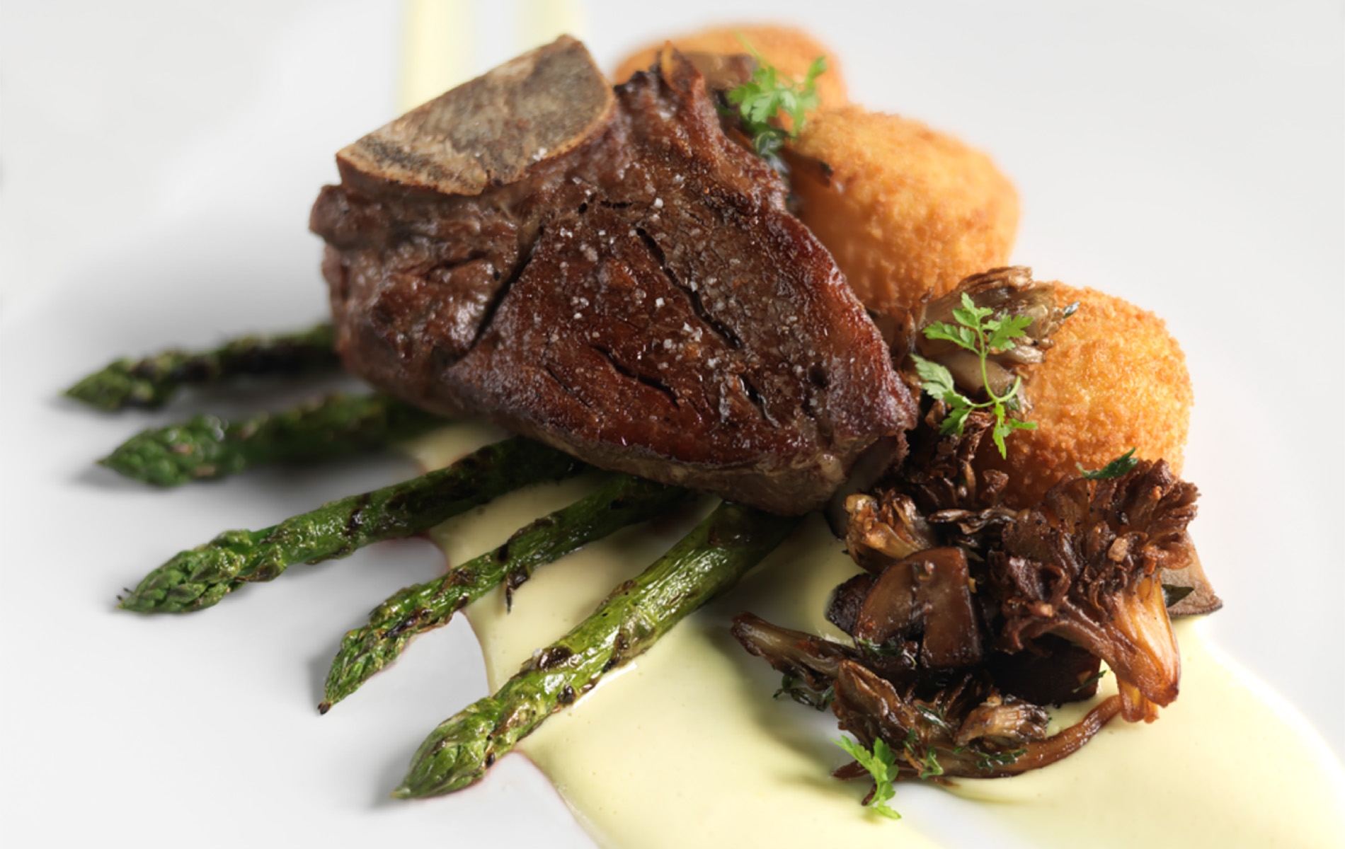 steak on top of green asparagus and a cream puree on a white plate