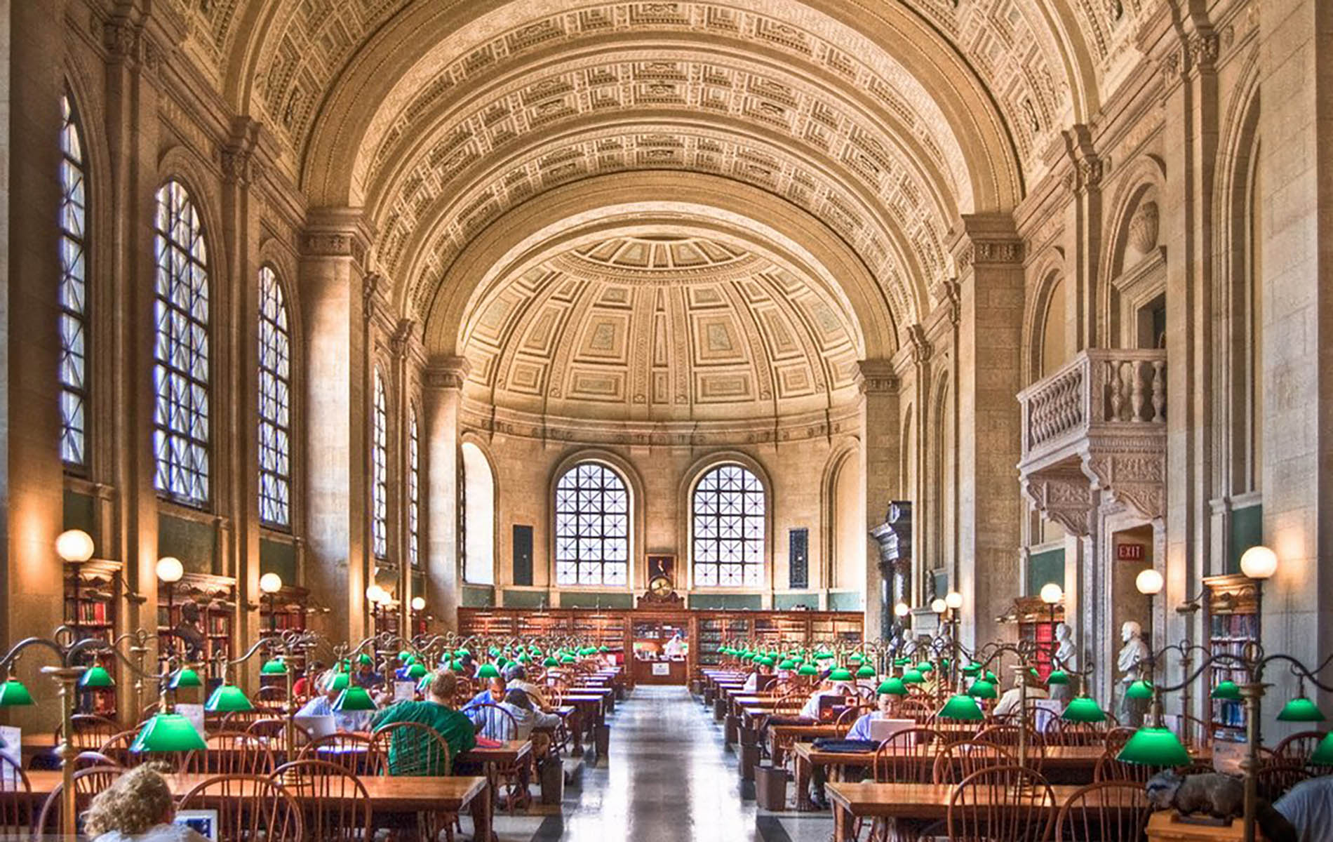 grand library with ornate white dome celling and two rows of wooden desk with green lamps