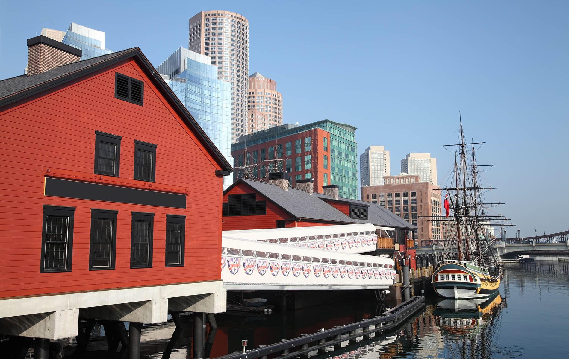 red building on a wharf with white railing walkway to boston tea party ship in water with clear blue sky