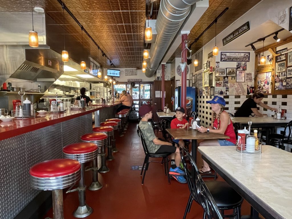 diner with 6 red stools on left and family on right 1 mom and two boys sitting at table