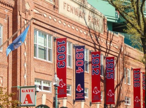 Sunset view of Fenway Park in Boston with the iconic red and white brick stadium facade with blue and red banners and surrounding city skyline