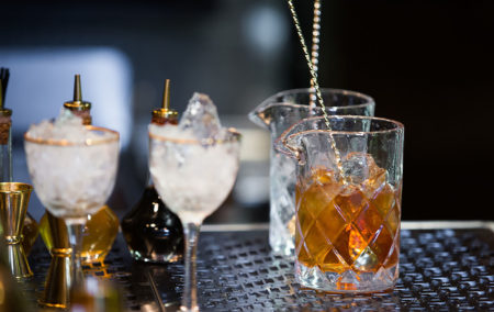 wo small chalices with ice and a cross hatched glass with bourbon on a bar