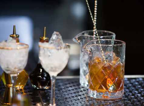 wo small chalices with ice and a cross hatched glass with bourbon on a bar