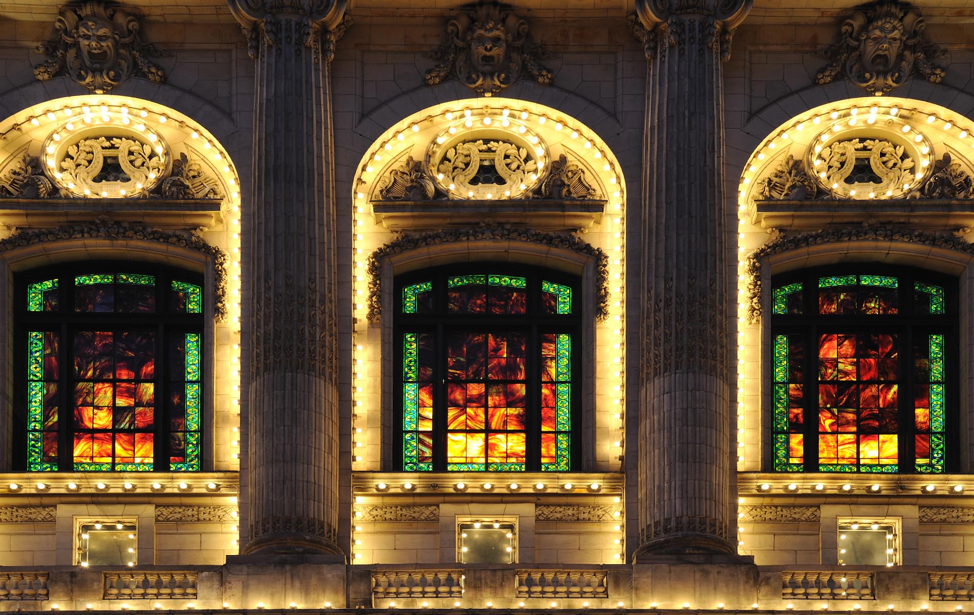 Three illuminated windows with stain glass red green and yellow a panels on ornate building