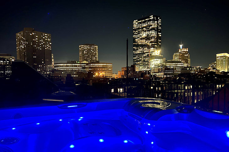 Bright blue water in hot tub on roof with city skyline view.