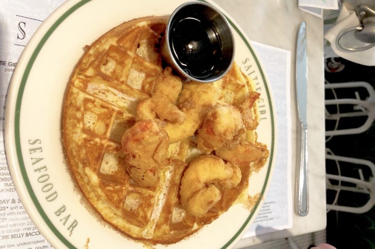 giant waffle topped with fried lobster and side of maple syrup in silver cup