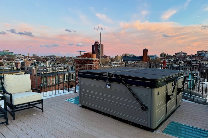 Boston hotel with hot tub on roof with tan deck and sun setting skyline.