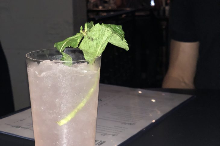 a pink cocktail with a spring of green mint next to a white menu that says black lamb