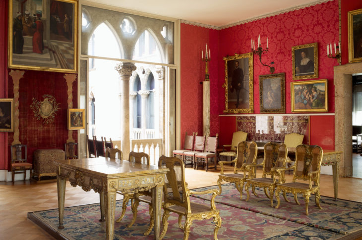 red room with 6 gold chairs in the center and two gothic arches in the background