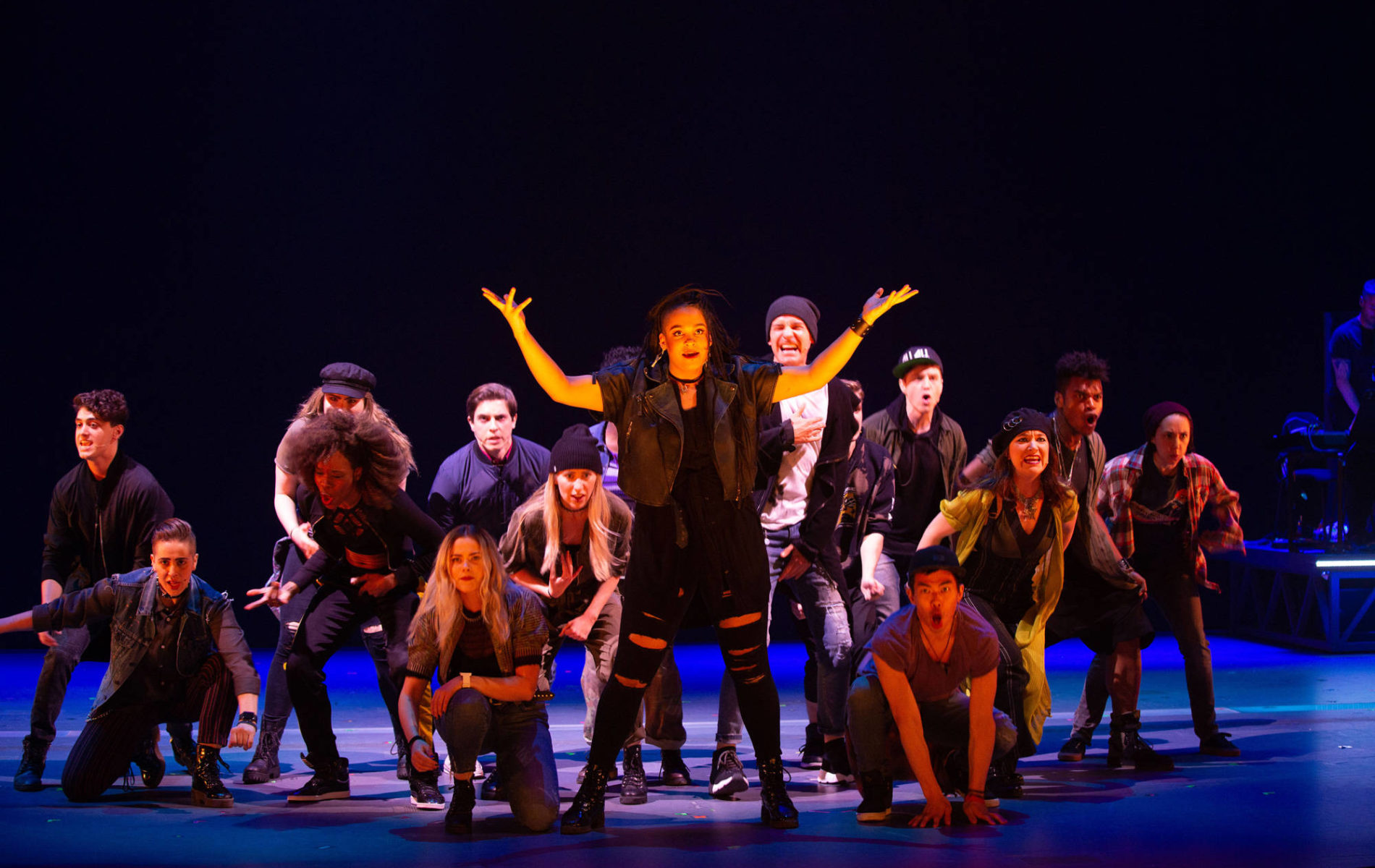 Cast performing on stage with blue lights and black background