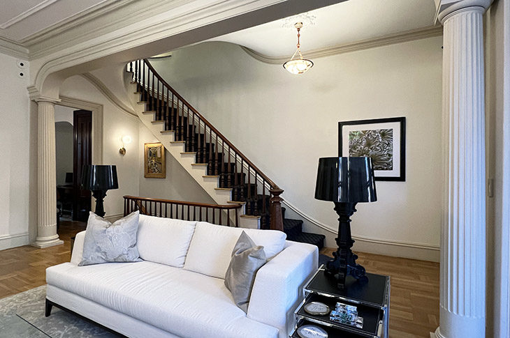 Victorian parlor with winding staircase, walnut railing. white walls, white sofa.