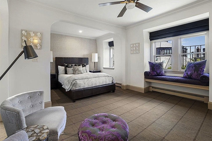 Bed with brown headboard, purple pillows and silver duvet - two side lamps and silver wallpaper.