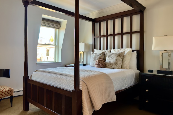 Modern and stylish guest room with mahogany 4 poster bed, tan carpet and white walls.