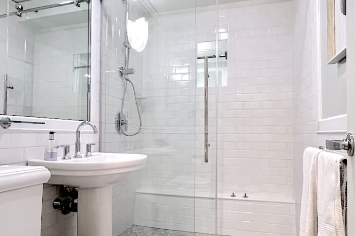 White tile bathroom with white marble floors, walk in shower and glass doors.