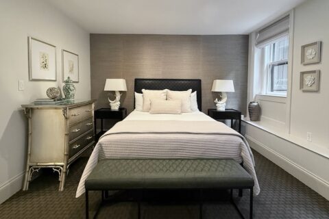 Bedroom with white walls, silver grass cloth wallpaper behind a black headboard. Dark green carpet and window onto garden.