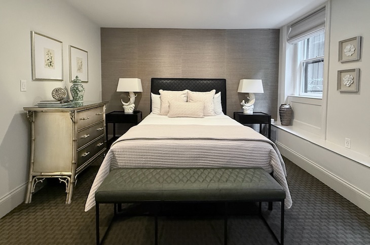 Bedroom with white walls, silver grass cloth wallpaper behind a black headboard. Dark green carpet and window onto garden.