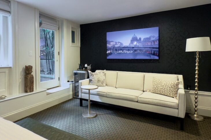 Bedroom with white walls, black wallpaper behind a white sofa. Dark green carpet and door onto garden.