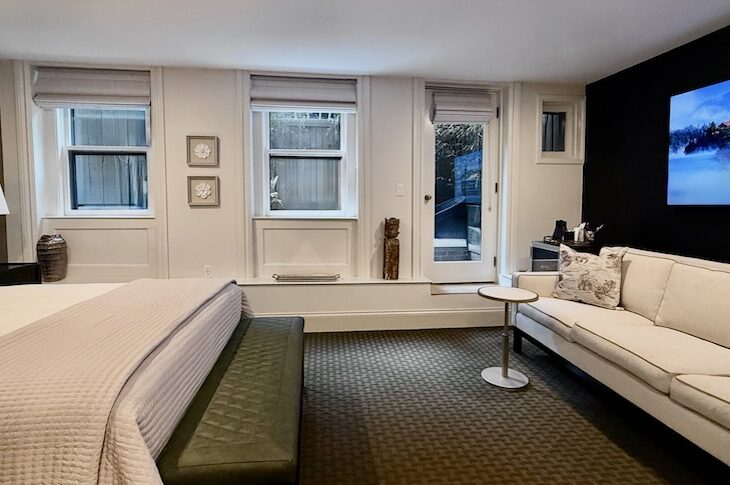 Bedroom with white walls, black wallpaper behind a white sofa. Dark green carpet, two windows and door onto a bamboo garden.