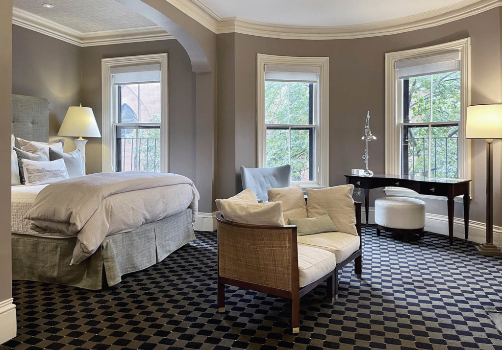 Spacious room with light green upholstered headboard, tall windows, sitting area with settee and mahogany desk