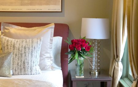 bed with two white and gold pillows with red head board and table with dozen red roses