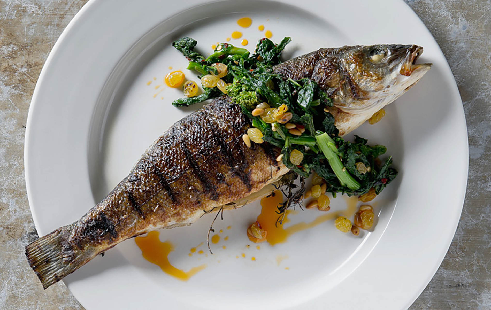 whole grilled fish on a white plate with greens on top