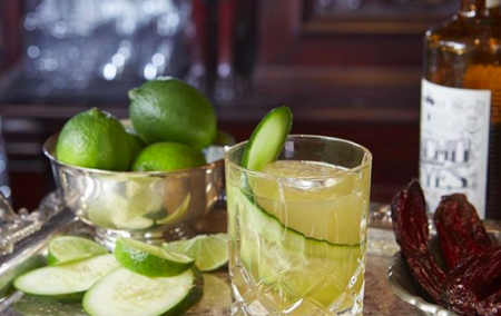 Margarita in a fancy glass with a silver bowl with 3 limes and a pile of dried chiles