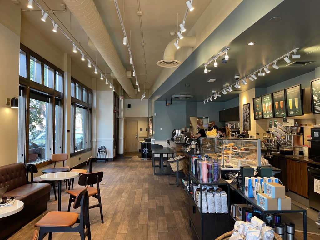 two window on the left with two chairs with orange fabric a wood floor and a counter of coffee shop on right