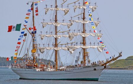tall ship with two mast with rolled up white sails and colorful flags