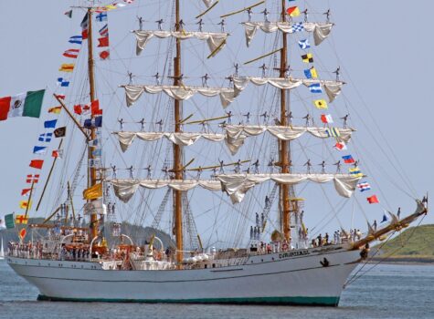 tall ship with two mast with rolled up white sails and colorful flags