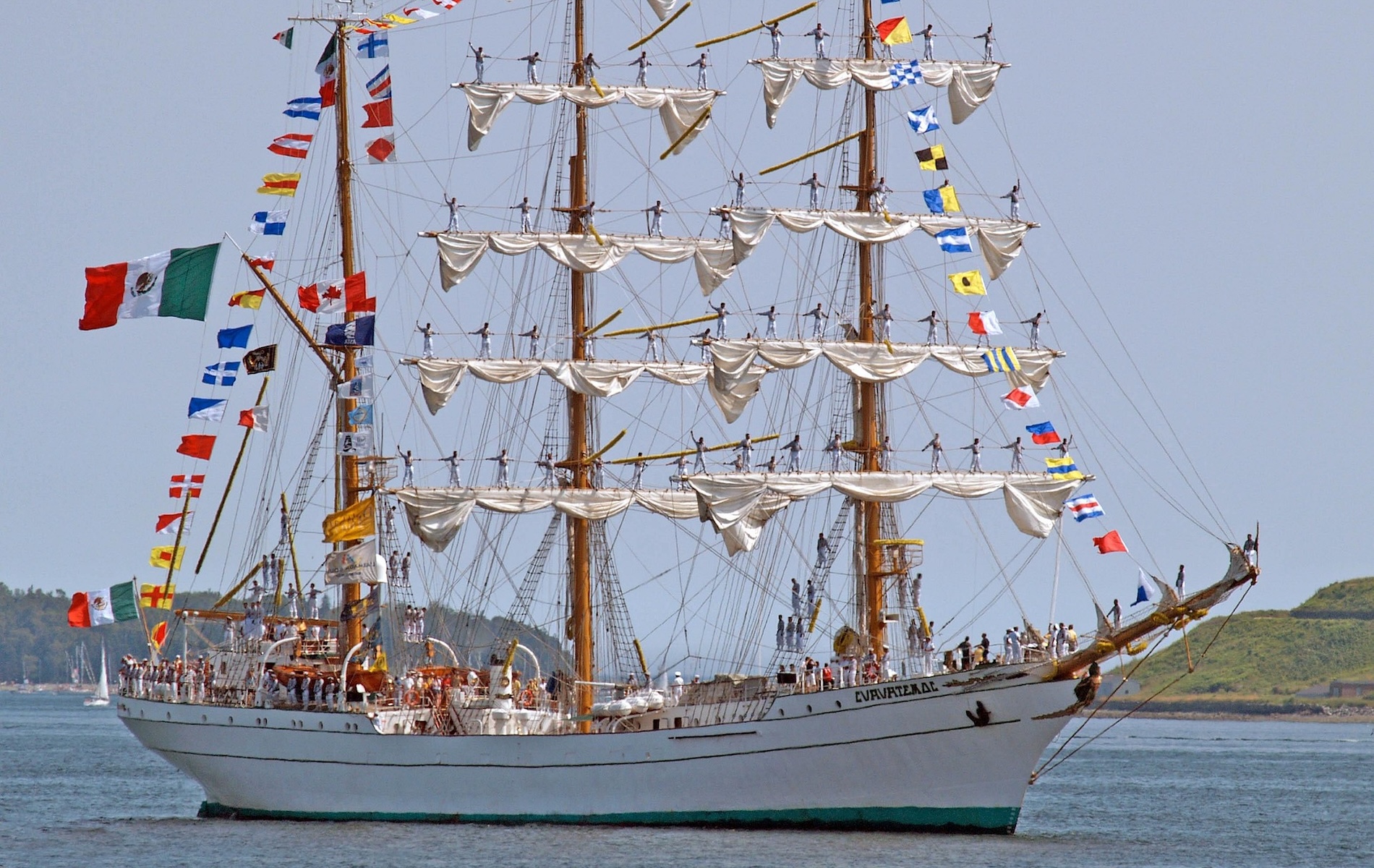 tall ship with two mast with rolled up white sails and colorful flags