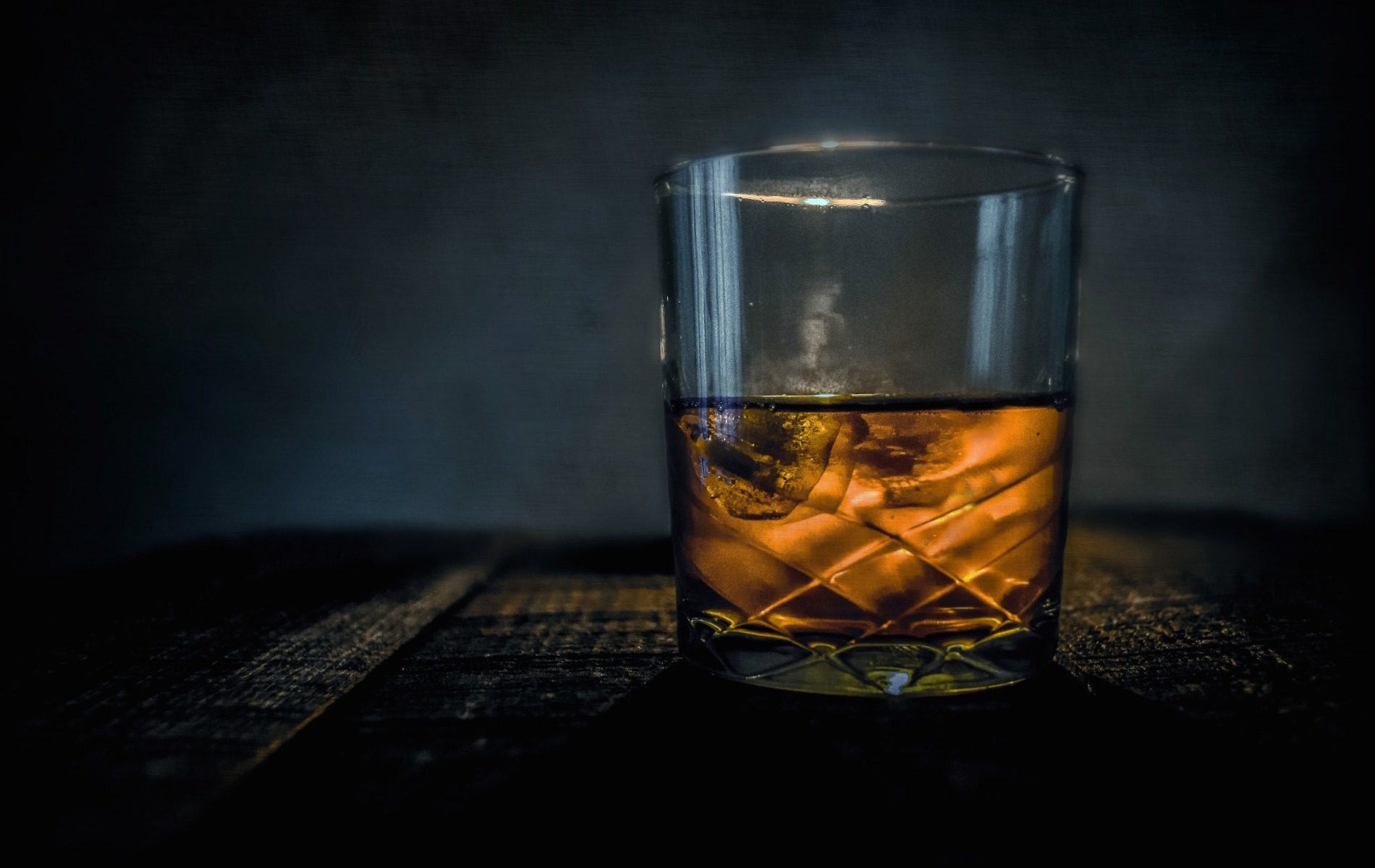 a cut crystal glass filled with golden brown whiskey on black background