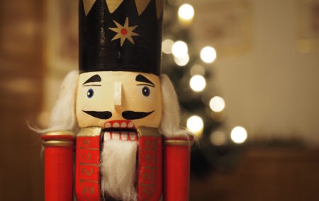 close up of a wooden nutcracker toy with black hat white beard and red body out of focus white lights behind
