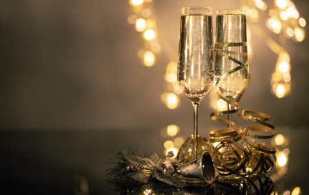 two glasses on champagne on the right with yellow lights behind and curled ribbon at base of glass