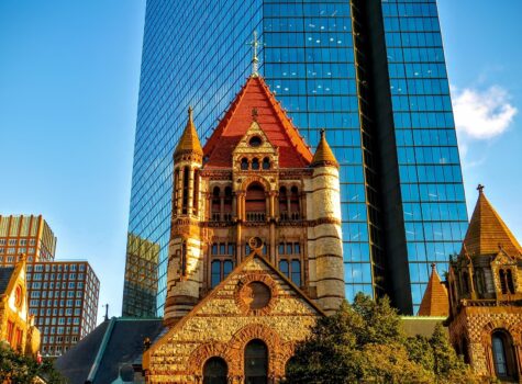 blue glass skyscraper with ornate orange church with greenery or trees on left and right
